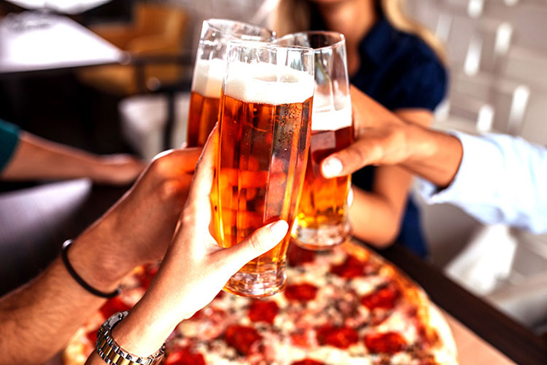 group cheers with beer while eating at pizza restaurant