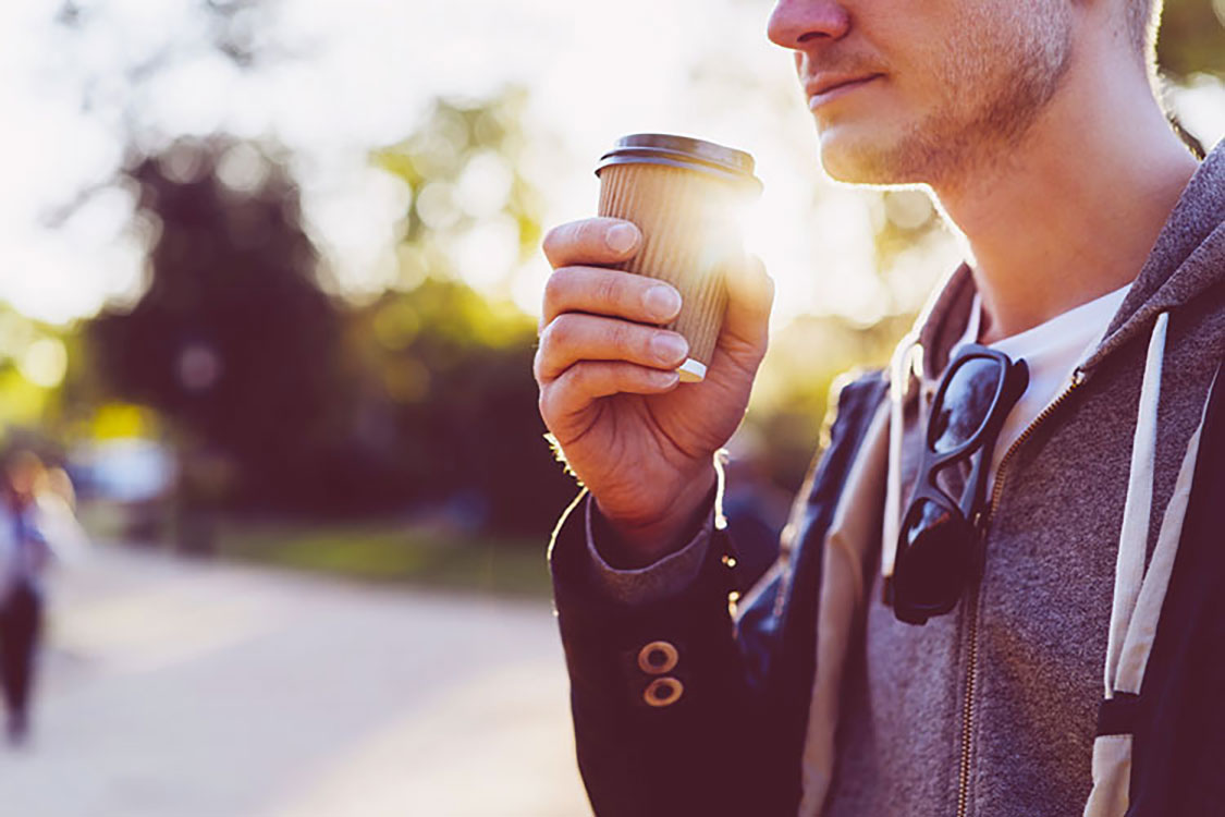 man smiling and drinking coffee on the go